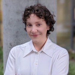 Portrait photo of Ella in a white shirt, standing outdoors against a blurred background.