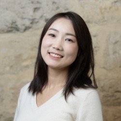 Dr Haiou Zhu, smiling at the camera, photographed against a stone wall.