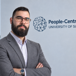 Lampros, AI student in a suit standing in front of the People-Centred AI centre. 