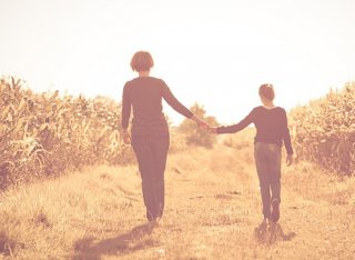 A mother and daughter walking hand in hand through a golden field