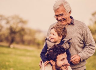 A young man with his son on his shoulders next to his older father