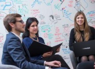 A man and two women sitting in a group in front of a full whiteboard with laptops