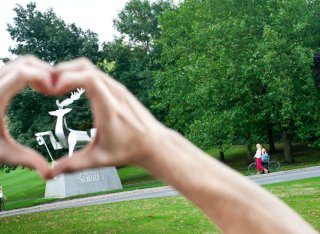 A student makes heart hands around the University of Surrey's stag statue on campus