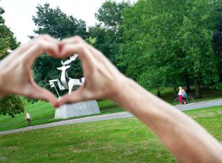A student makes heart hands around the University of Surrey's stag statue on campus