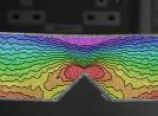 Example of output from DIC – here, a notched specimen is placed in four point bending, with the notch in the tensile face. The image shows the intensity of the tensile and compressive forces at the surfaces, decreasing to zero at the neutral axis, but concentrated at the tip of the notch.