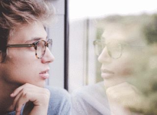 Male with glassess looking at his reflection iin glass