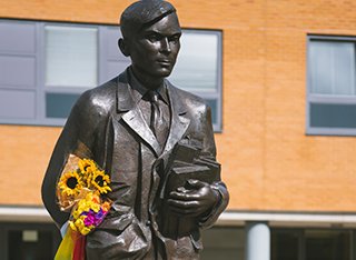 Alan Turing statue with pride flag, candles and flowers