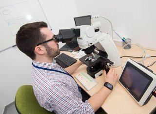 A man in a checked shirt looking into a microscope