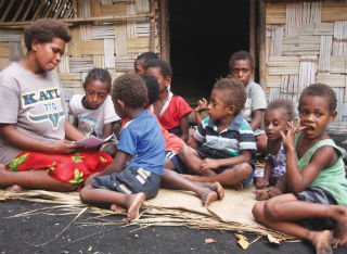 A kindergarten teacher reads stories outside to a group of Vanuatu school children
