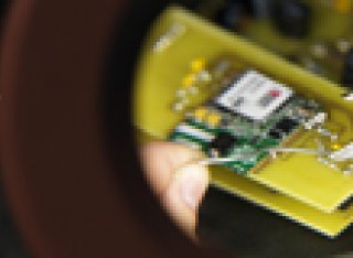 Looking through a magnifying glass at tweezers putting together an electrical board