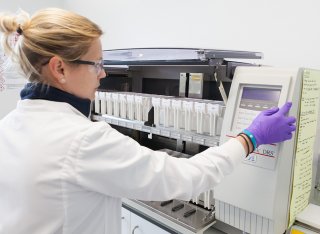 A women wearing a white coat and purple gloves is operating a stainer