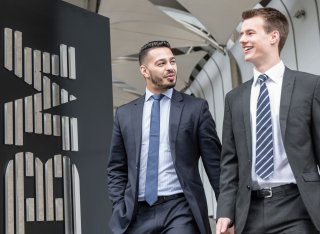 Two males in suits walking next to IBM sign.