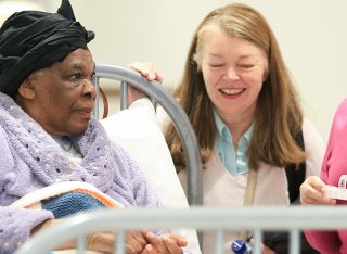 An elderly lady is sitting in bed surrounded by friends