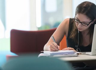 Female student studying the Library writing in a notebook