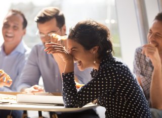 A small group of colleagues seated around a table laugh together