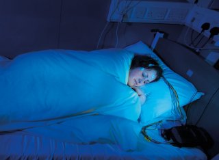 Woman sleeping in a bed with monitors and a blue light on