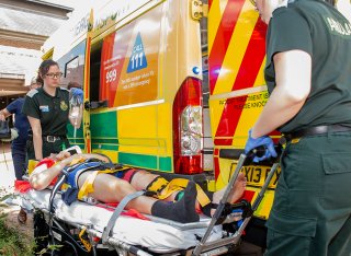 Paramedic sciences students wheeling an actor-patient into an ambulance