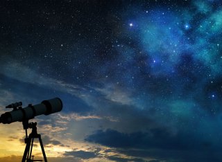Telescope on hill at night with stars shining