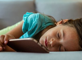 A young girl is asleep in front of a mobile phone