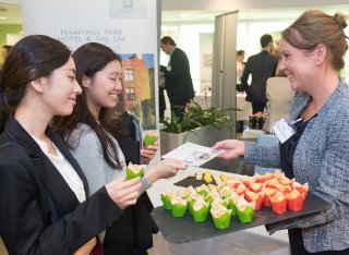 Two female students taking a card from a prospective employer