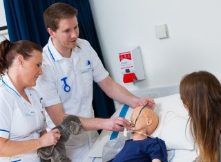 Two nursing students treating a child mannequin while talking to a parent