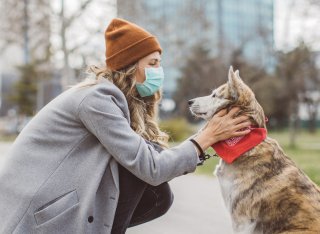 Woman wearing a PPE mask bent down petting her dog