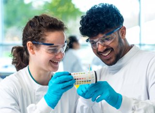 Two students holding a tub of litmus paper with pH scale on the side