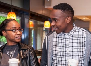 A black woman and man are in conversation with coffee cups in their hand