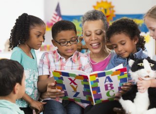 School children standing around their teacher who is reading a book