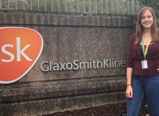 Biosciences student, Chloe Charlwood, standing in front of a GlaxoSmithKline (GSK) sign