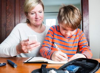 Mum watching her son write down his blood glucose levels in a notebook