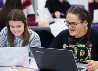 Two students on laptops laughing