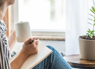 Woman holding a pen and pad in one hand and a mug in the other