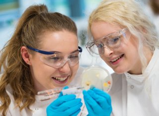 Two students holding an agar plate and measuring bacterial growth