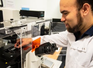 Student in lab coat standing by a microscope using scientific equipment