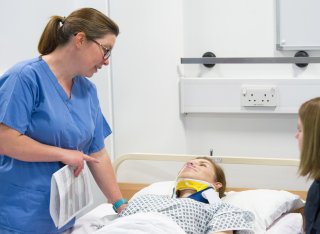 Nurse speaking to a woman wearing a neck brace, laying in a bed