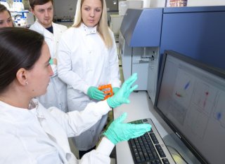 Demonstrating Flow Cytometer to students, close up of students sat round talking