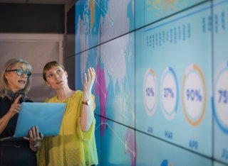 Two women discussing data on a giant screen to represent knowledge exchange
