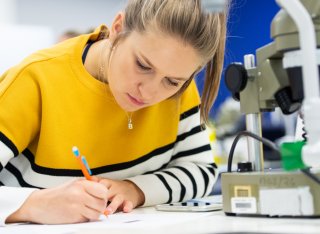 Student writing on a piece of paper next to a microscope