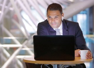 Man in a suit sat at a table and watching something on his laptop