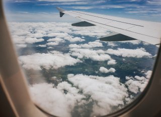 The view of clouds and an aircraft's wing, seen through the oval window of a plane from the interior