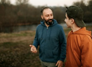 A man and boy talk as they walk through a green space