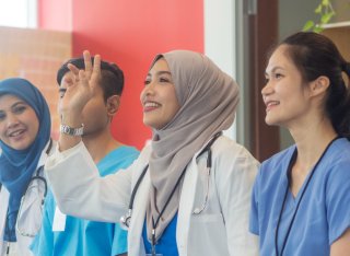 A group of Malaysian medical staff having a meeting. It is a medical team with four people from different ethnic backgrounds attending a medical conference. A Muslim female doctor raises her hand