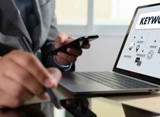 Person in suit on their mobile with the word 'keyword' up on their laptop screen