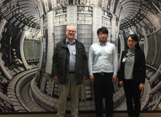 Three scientists stand in front of an image of a nuclear reactor