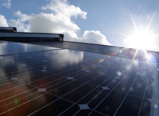 The sun glints off some solar panels in front of a blue sky studded with fluffy clouds