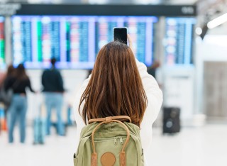Young women taking photo of departures board with mobile phone