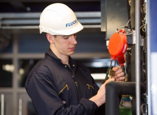 A chemical engineering student with a white hard hat on secures a padlock in the Fluor Pilot Plant.
