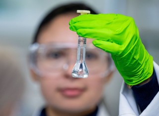 A Pharmaceutical Sciences student in bright green gloves holds up a sample