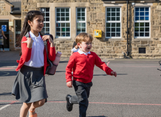 two children run across a primary school playground